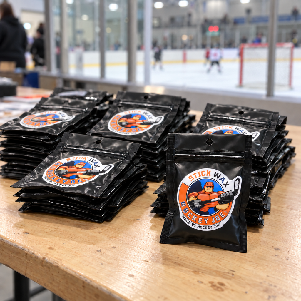 Hockey Joe wax giveaway pouches stacked on a table beside an ice rink, with one pouch standing in front