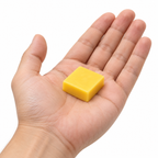Yellow Hockey Joe wax piece resting in an adult palm — approximate size illustration, 1¼ inches across and ½ inch thick